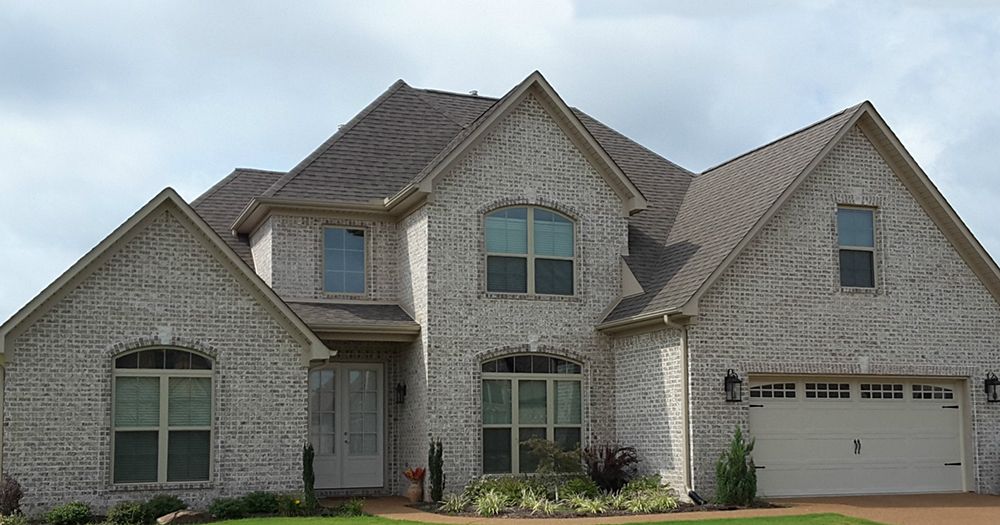 Two-story brick house with a white garage door under a cloudy sky.