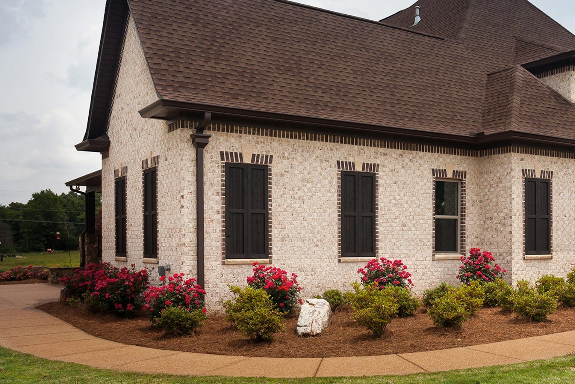 Brick house with brown roof, black shutters, and landscaping.