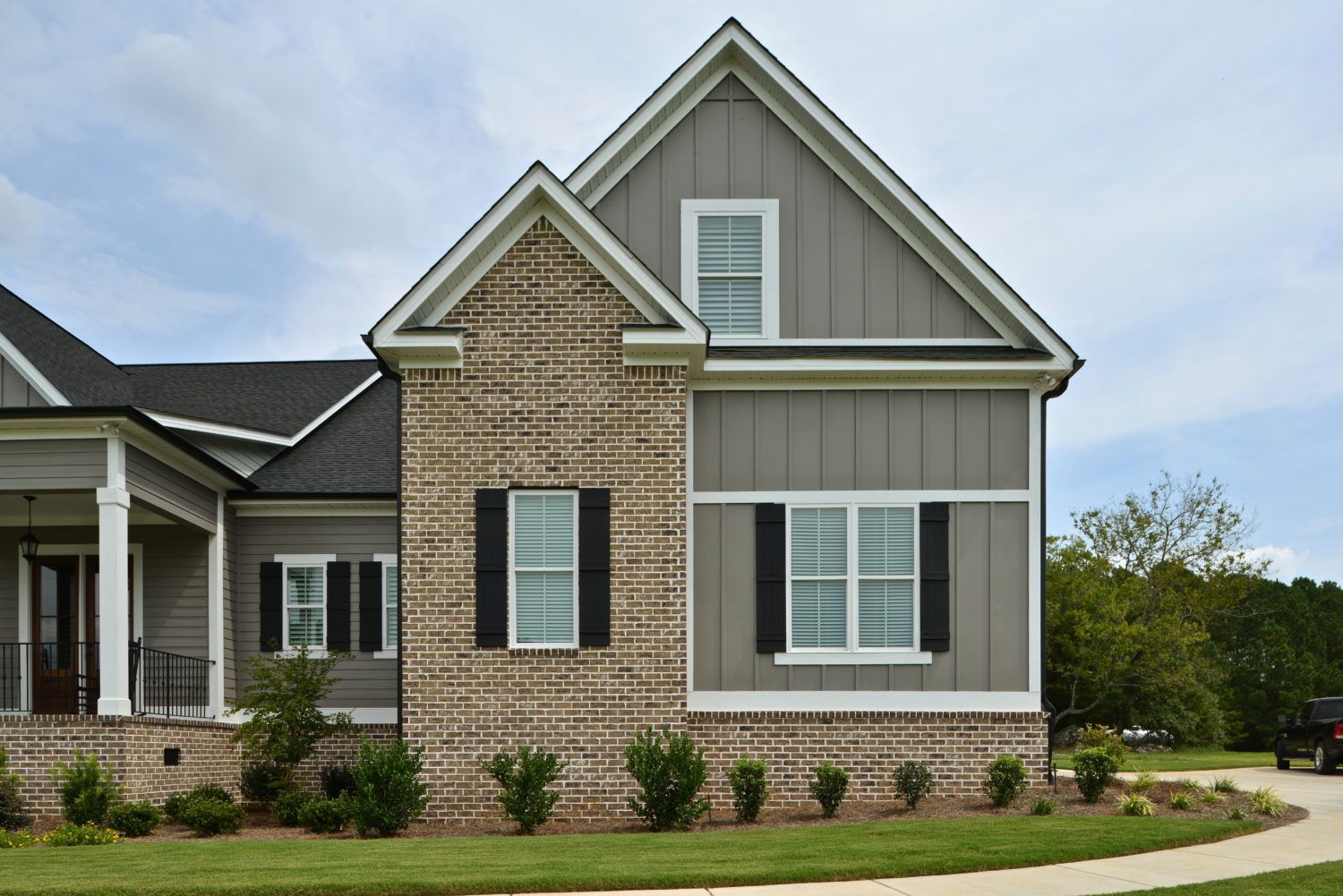 Two-story house with brick and gray siding, black shutters, and a lawn.