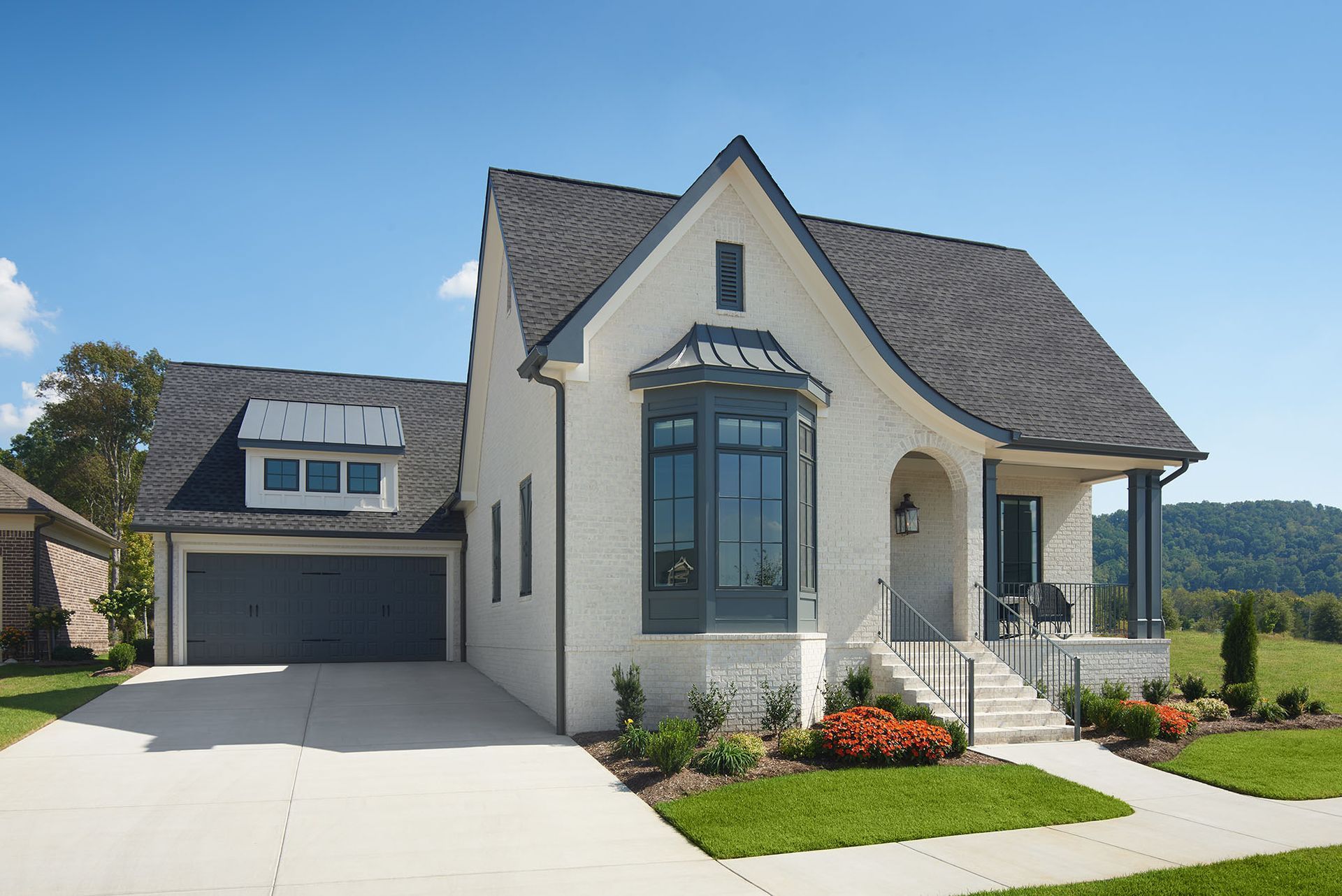White brick house with gray roof, garage, and front porch, set on a green lawn against a blue sky.