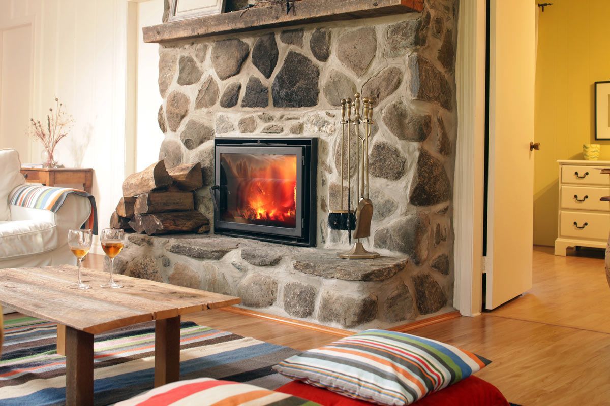 Fireplace with stone surround, lit fire, wooden mantel, and seating area with rug.
