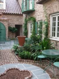 Brick courtyard with green accents, potted plants, and bistro set.