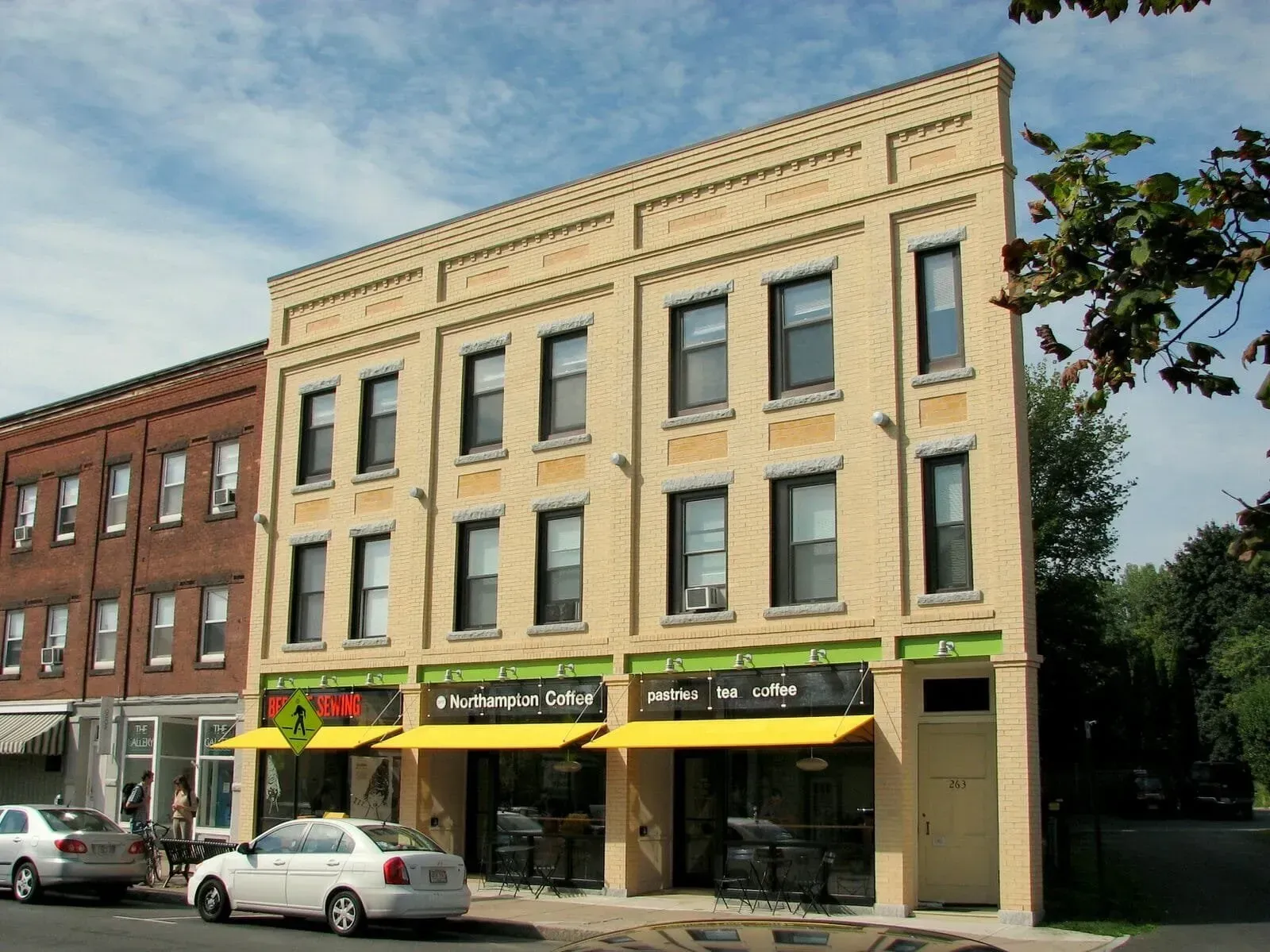 Three-story brick building with businesses on the ground floor, yellow awnings, and parked cars on the street.