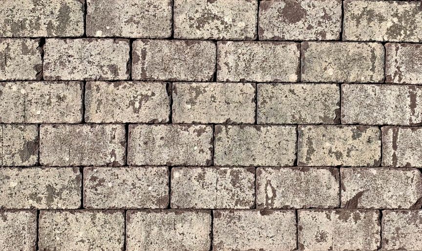 Gray rectangular paving stones arranged in a brick pattern, with faded, mottled appearance.