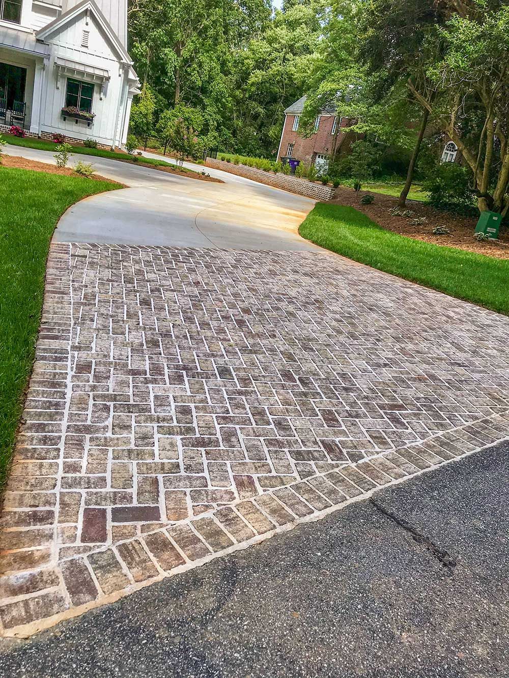 Brick driveway leading to a white house with green lawn.