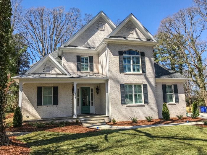 Two-story house with gray painted brick exterior, shutters, porch, and teal front door.