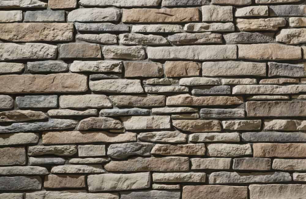 Stone wall with varied rectangular and irregular stones in tan, brown, and gray hues.