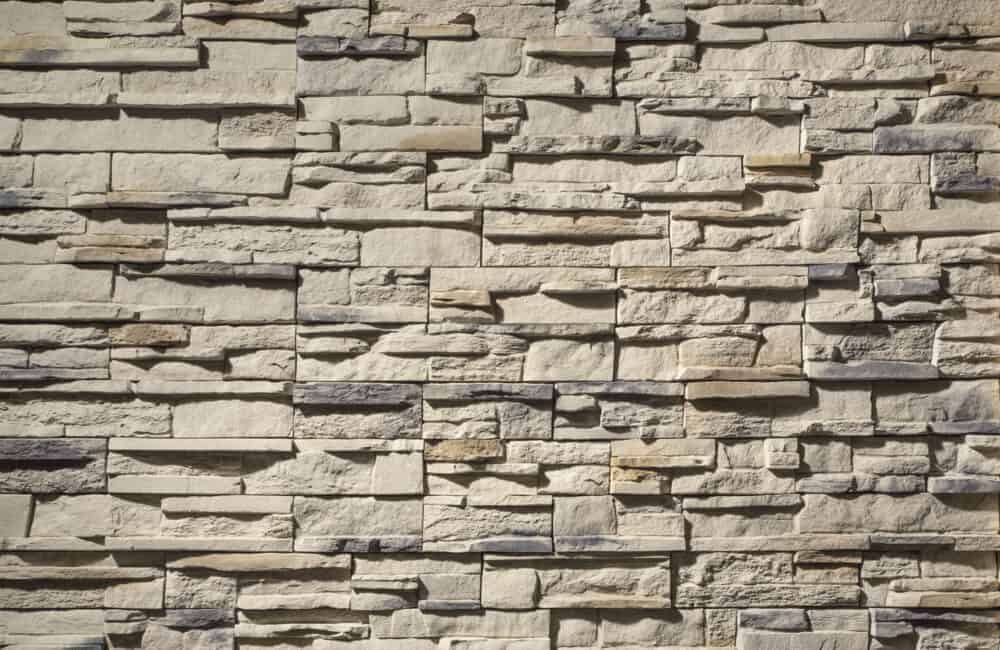 Textured, light-colored stone wall with varying shades and sizes of rectangular blocks.