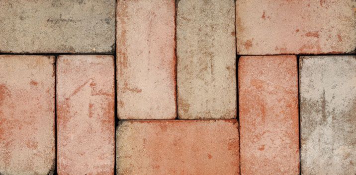 Close-up of weathered brick pavers in a herringbone pattern; various shades of red and tan.