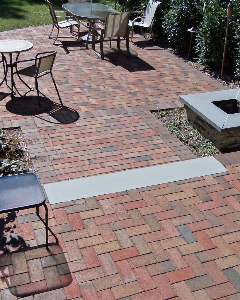 Brick patio with metal tables and chairs; square fire pit, and a long silver strip.