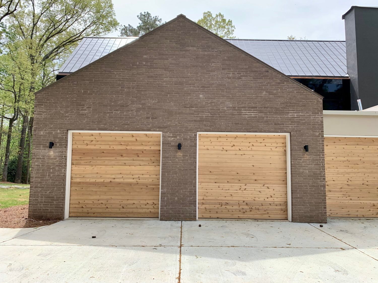 Brick garage with wooden doors; black metal roof in background.