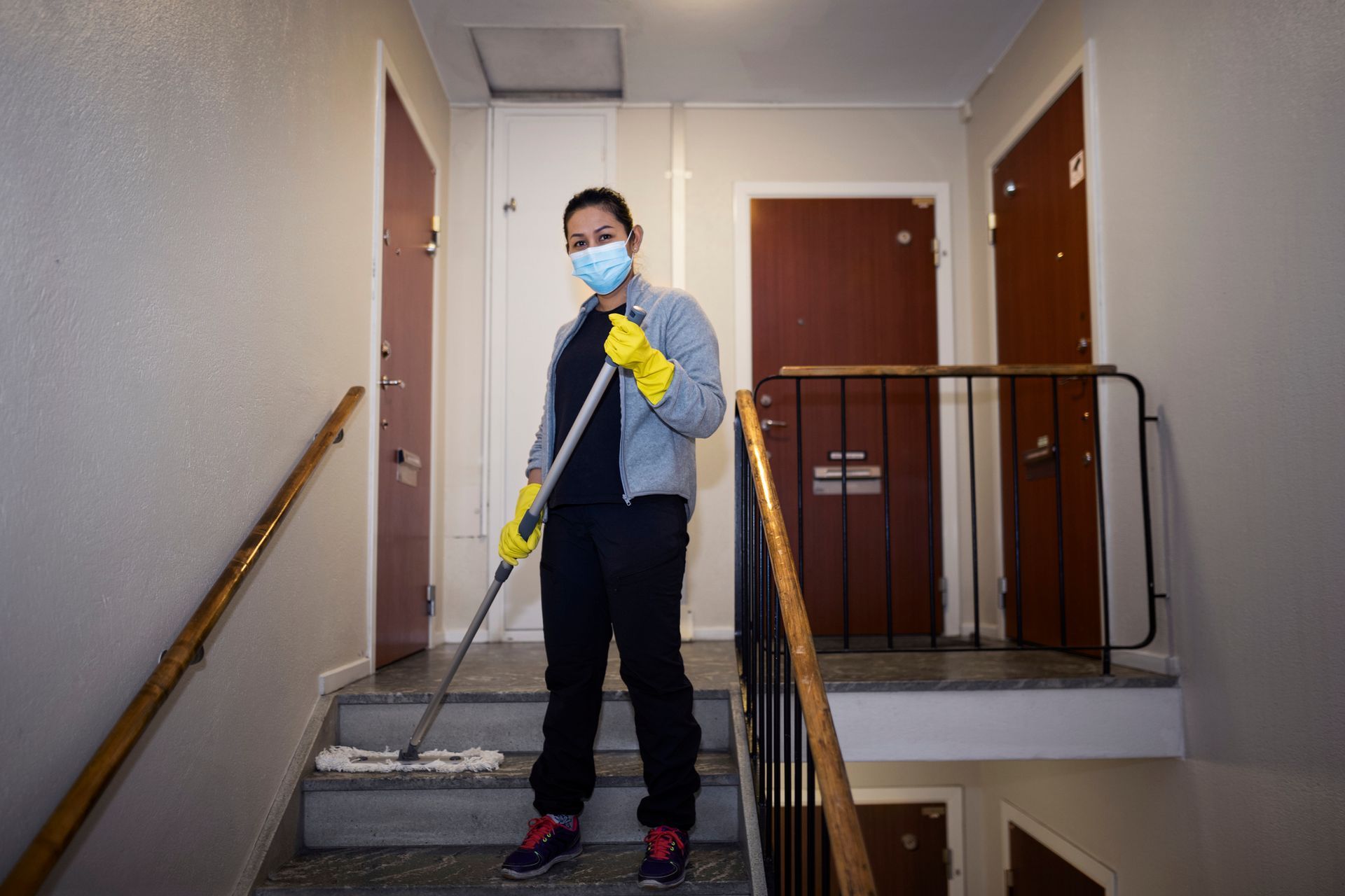 Una donna che indossa una maschera e guanti sta lavando le scale di un edificio.