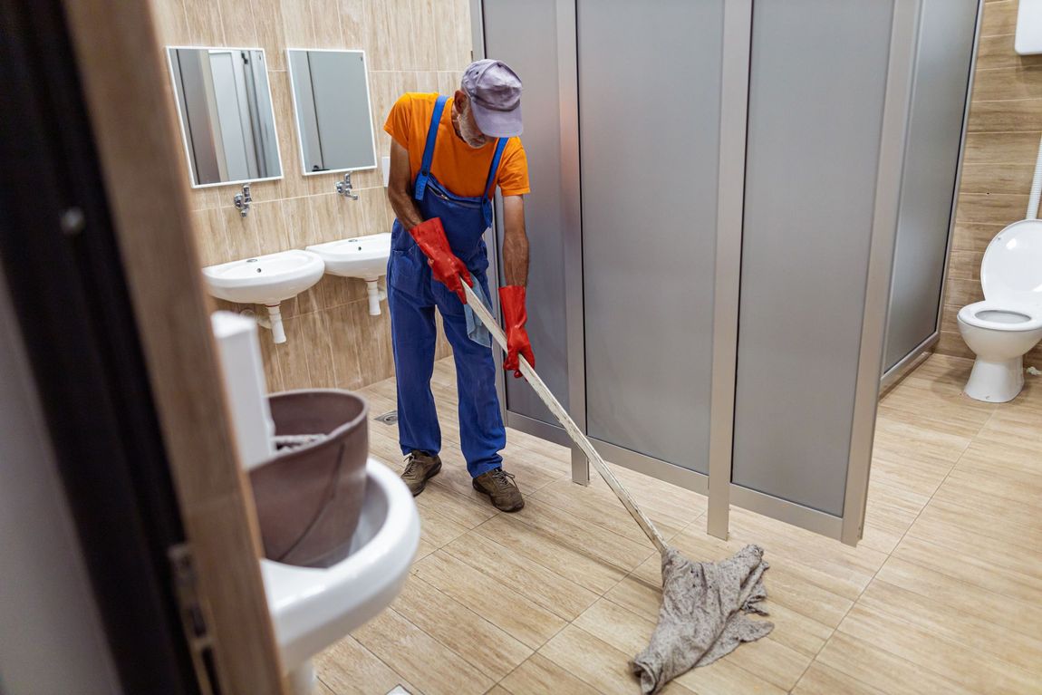 Un uomo sta pulendo il pavimento del bagno con uno spazzolone.
