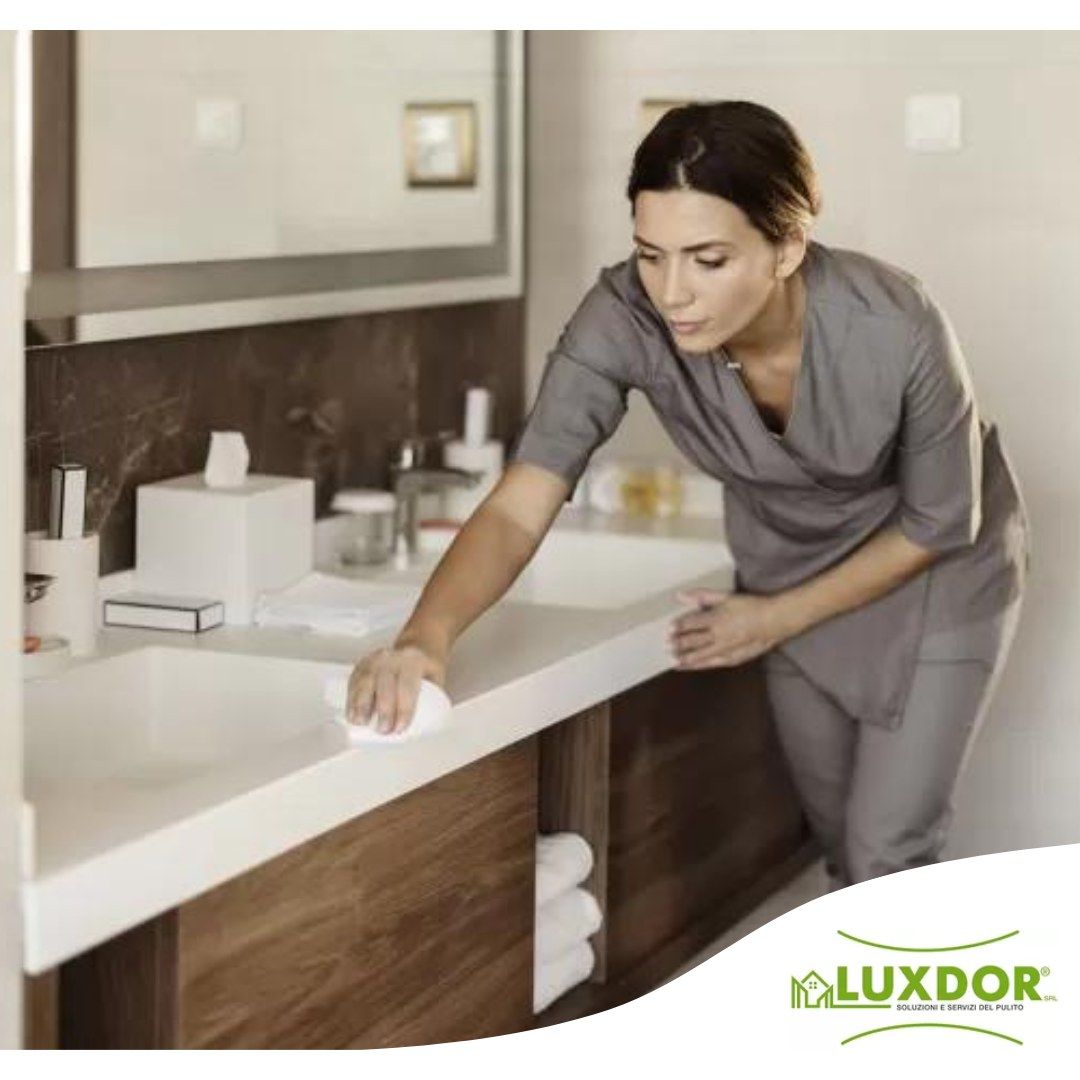 Una donna sta pulendo il bancone del bagno con il logo Luxdor nell'angolo