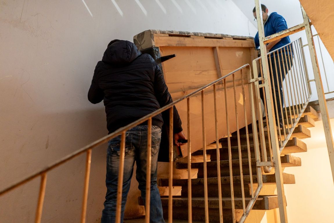 Due uomini trasportano una scatola di legno su per una rampa di scale.