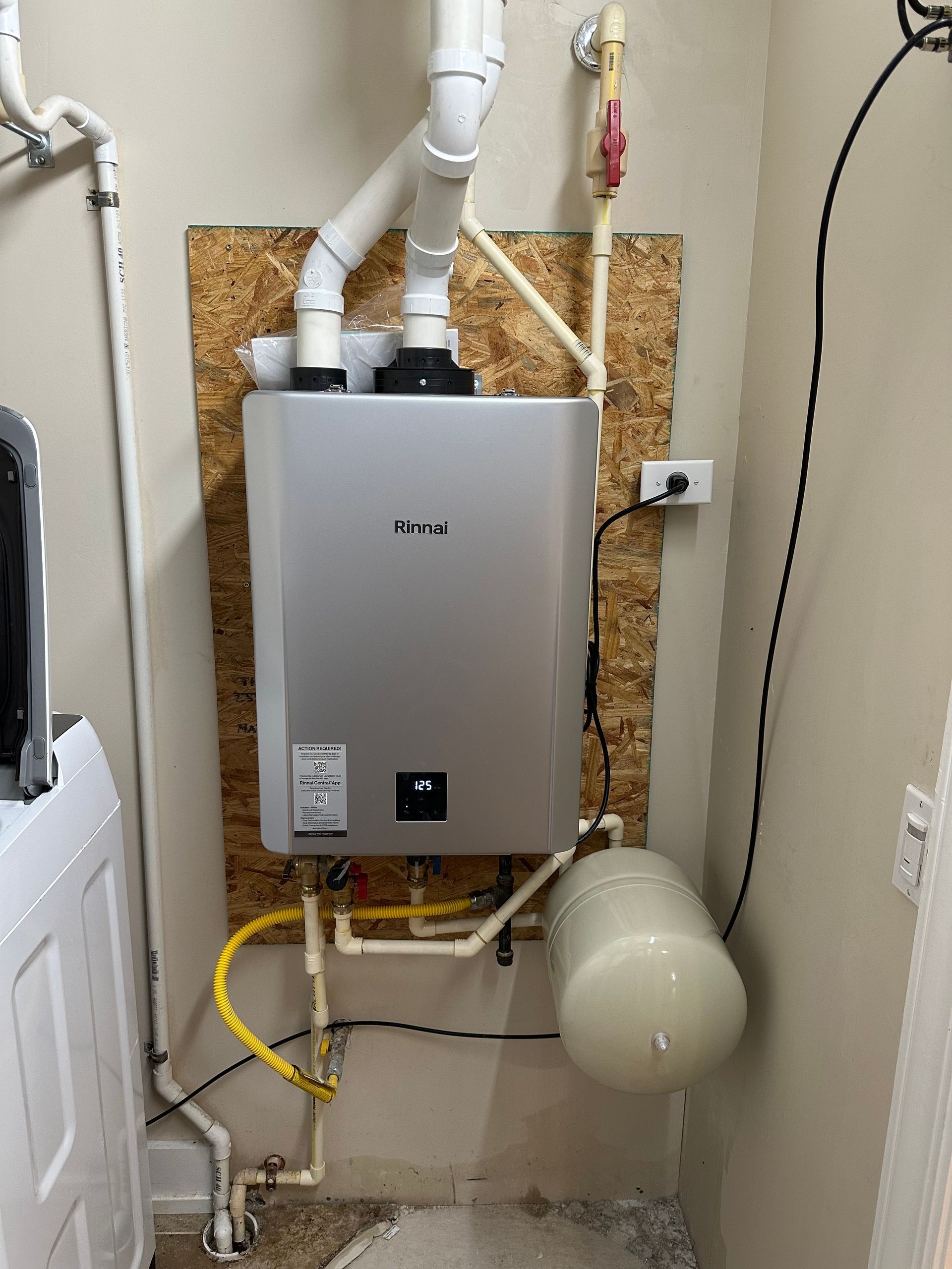Wall-mounted water heater with white pipes, pressure tank, and exposed utility area