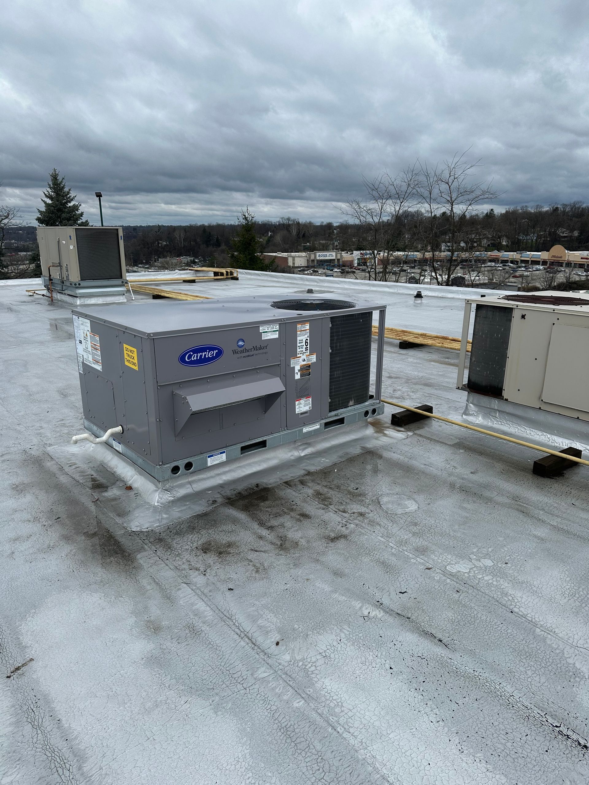Gray rooftop HVAC unit on a snowy rooftop under a cloudy sky.