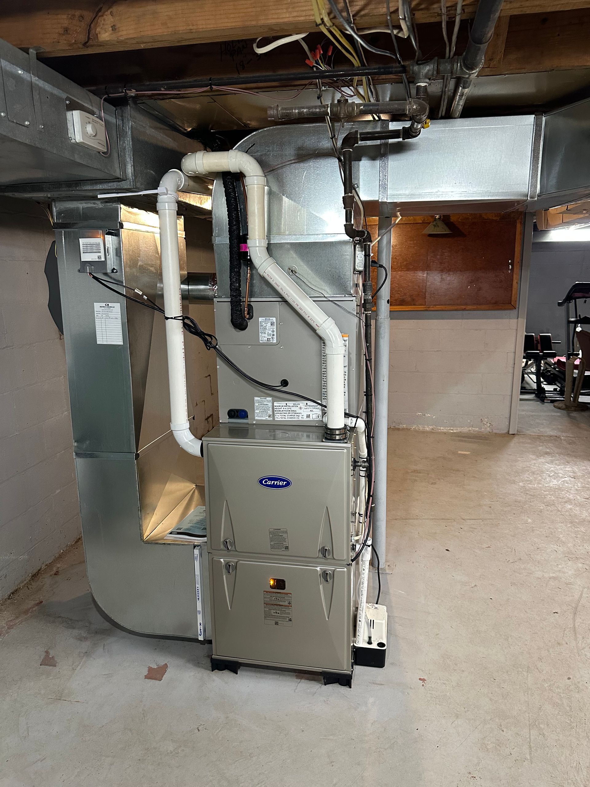 Basement HVAC furnace and ductwork in a utility room with exposed pipes and concrete floor