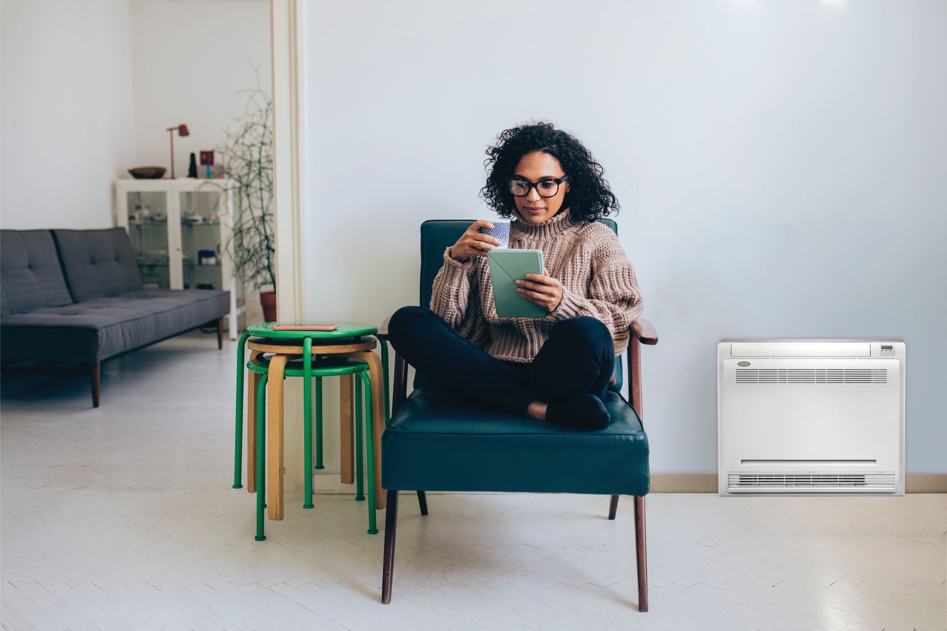 Person sitting in a teal armchair using a tablet in a minimalist living room