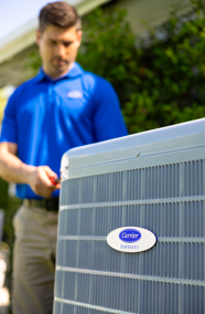 Technician in blue shirt inspecting a Carrier outdoor HVAC unit outdoors.