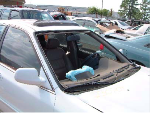 A white car with a broken windshield is parked in a lot