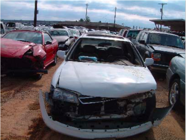 A white car with a damaged front bumper is parked in a lot with other cars