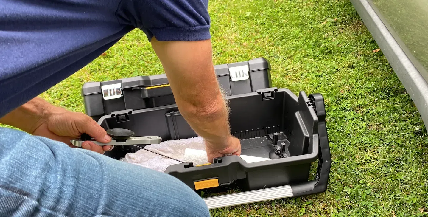 A man is kneeling down in the grass next to a toolbox.