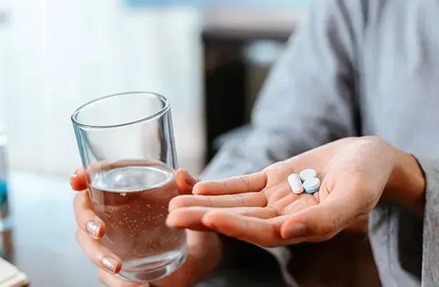 A person is holding a glass of water and a pill in their hand.