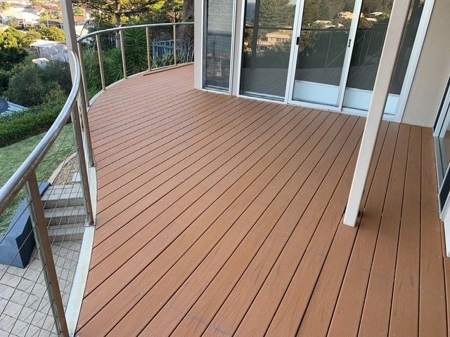 A wooden deck with a stainless steel railing and sliding glass doors.
