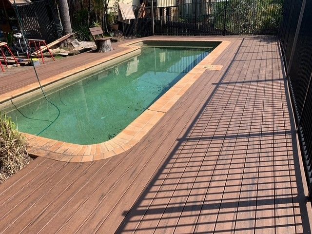 A large swimming pool with a wooden deck surrounding it.