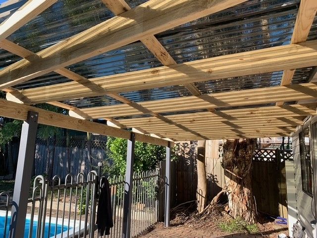 A wooden pergola with a clear roof is sitting next to a pool.