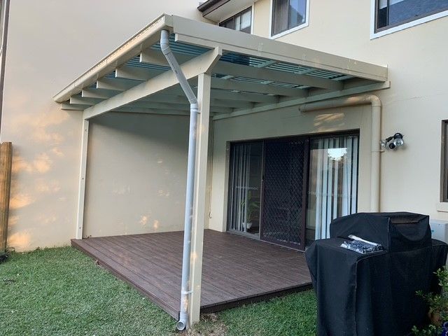 A patio with a pergola and a grill in the backyard of a house.