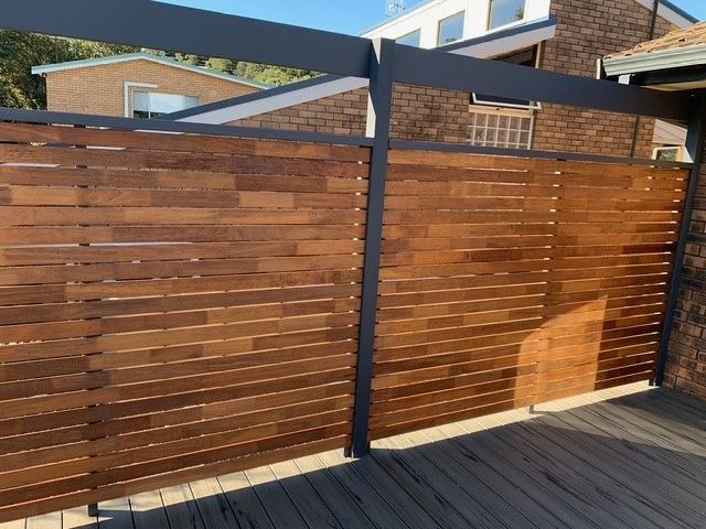 A wooden fence surrounds a deck with a brick building in the background.