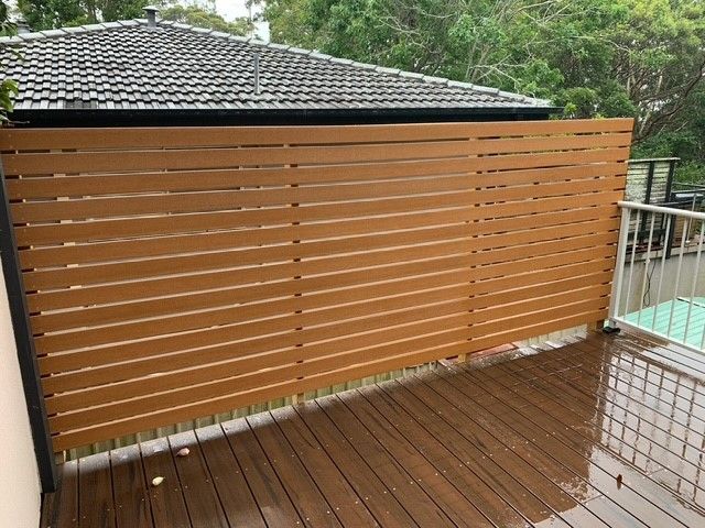 A wooden fence on a deck next to a house.