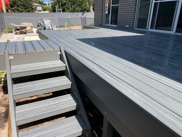 A gray wooden deck with stairs leading up to it.