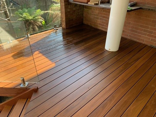 A wooden deck with a glass railing and a brick wall.