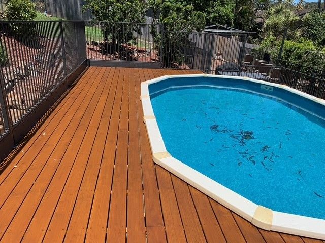 A wooden deck with a swimming pool in the background