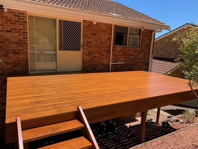 A wooden deck with stairs is in front of a brick house.