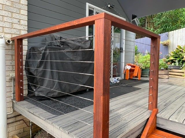 A wooden deck with a stainless steel railing and a motorcycle cover on it.