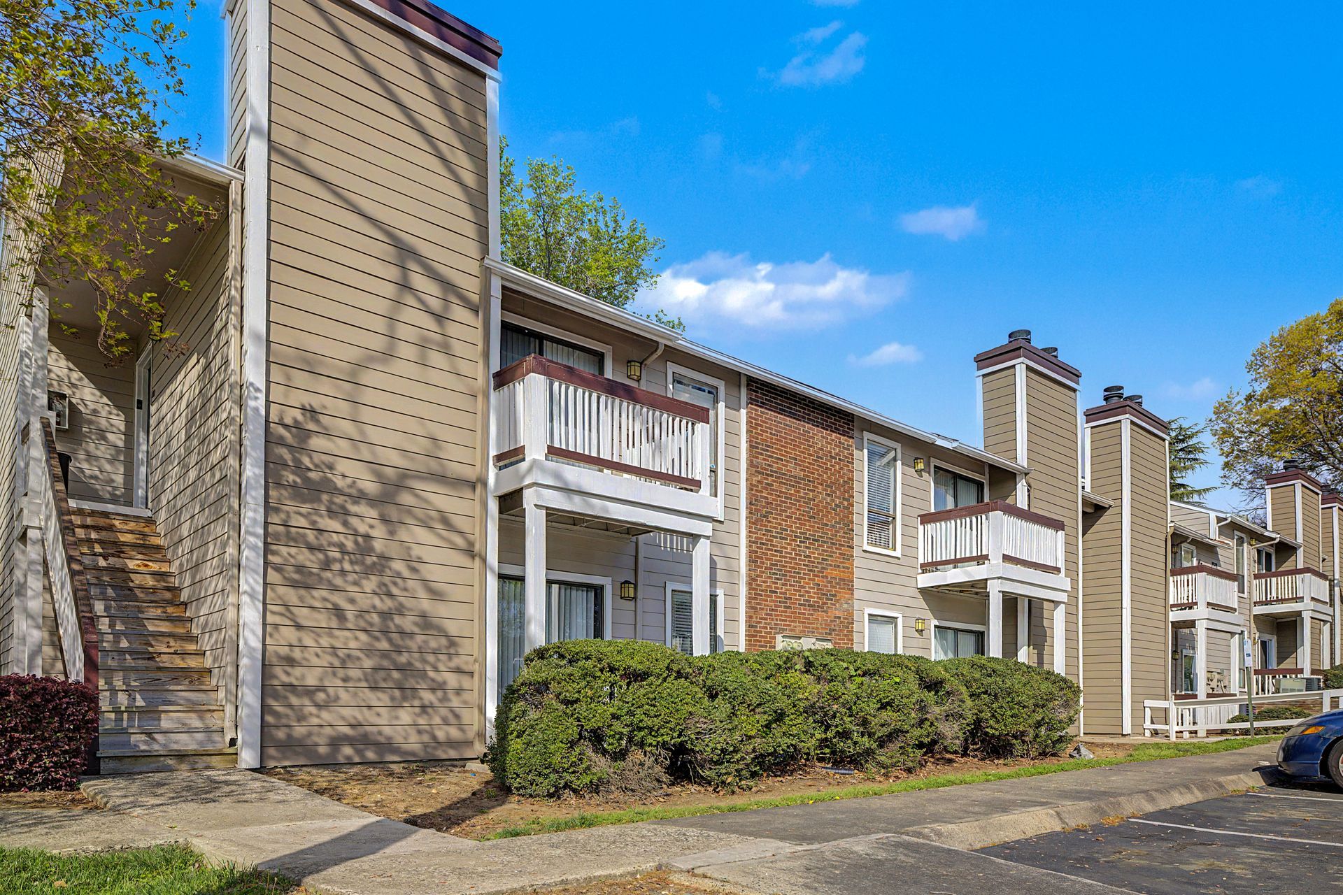 Apartment complex exterior with brick facades, balconies, and trees under a blue sky