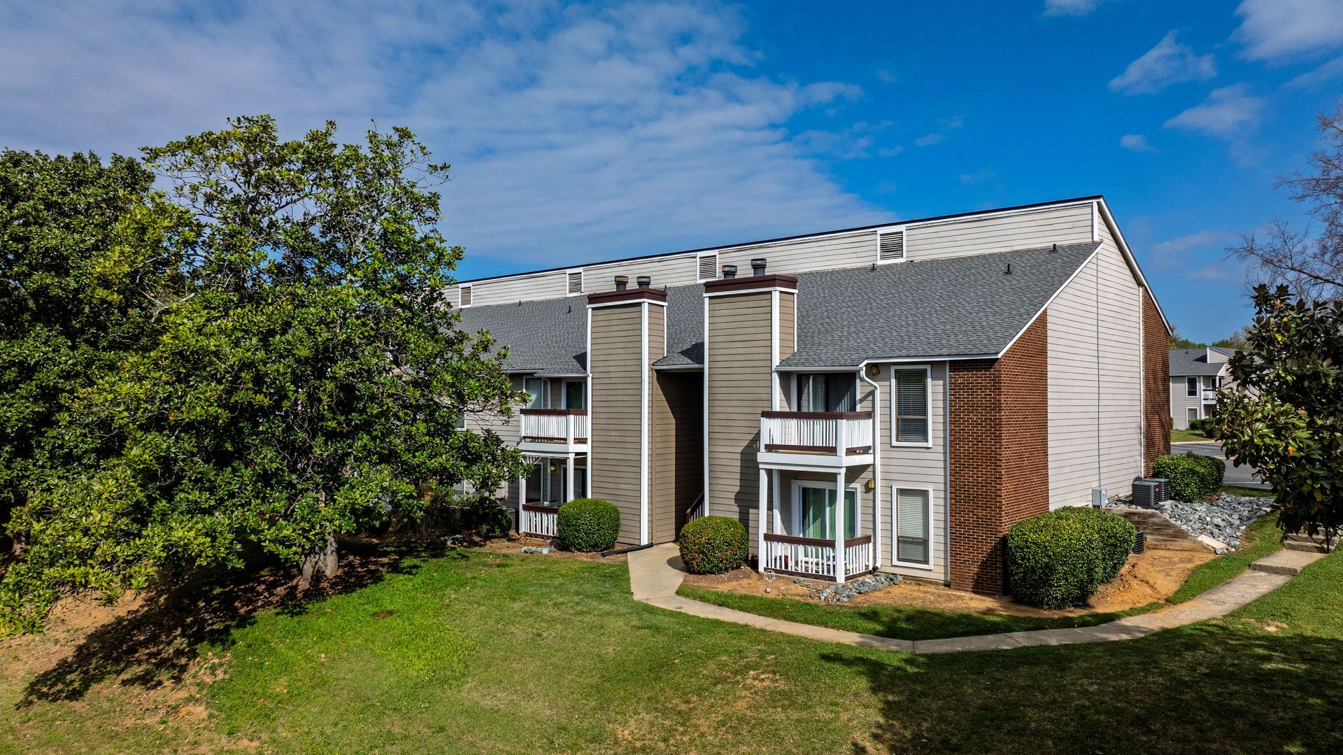 Apartment building with white balconies and brick walls beside a green lawn under a blue sky