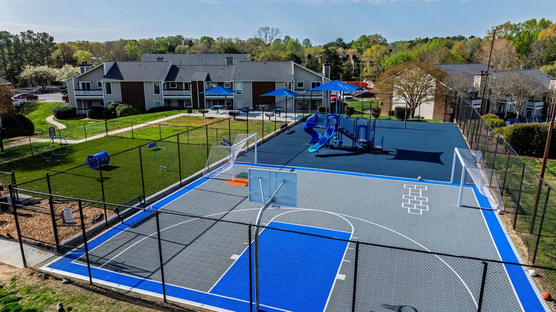 Aerial view of a blue-and-gray outdoor sports court beside houses and trees.