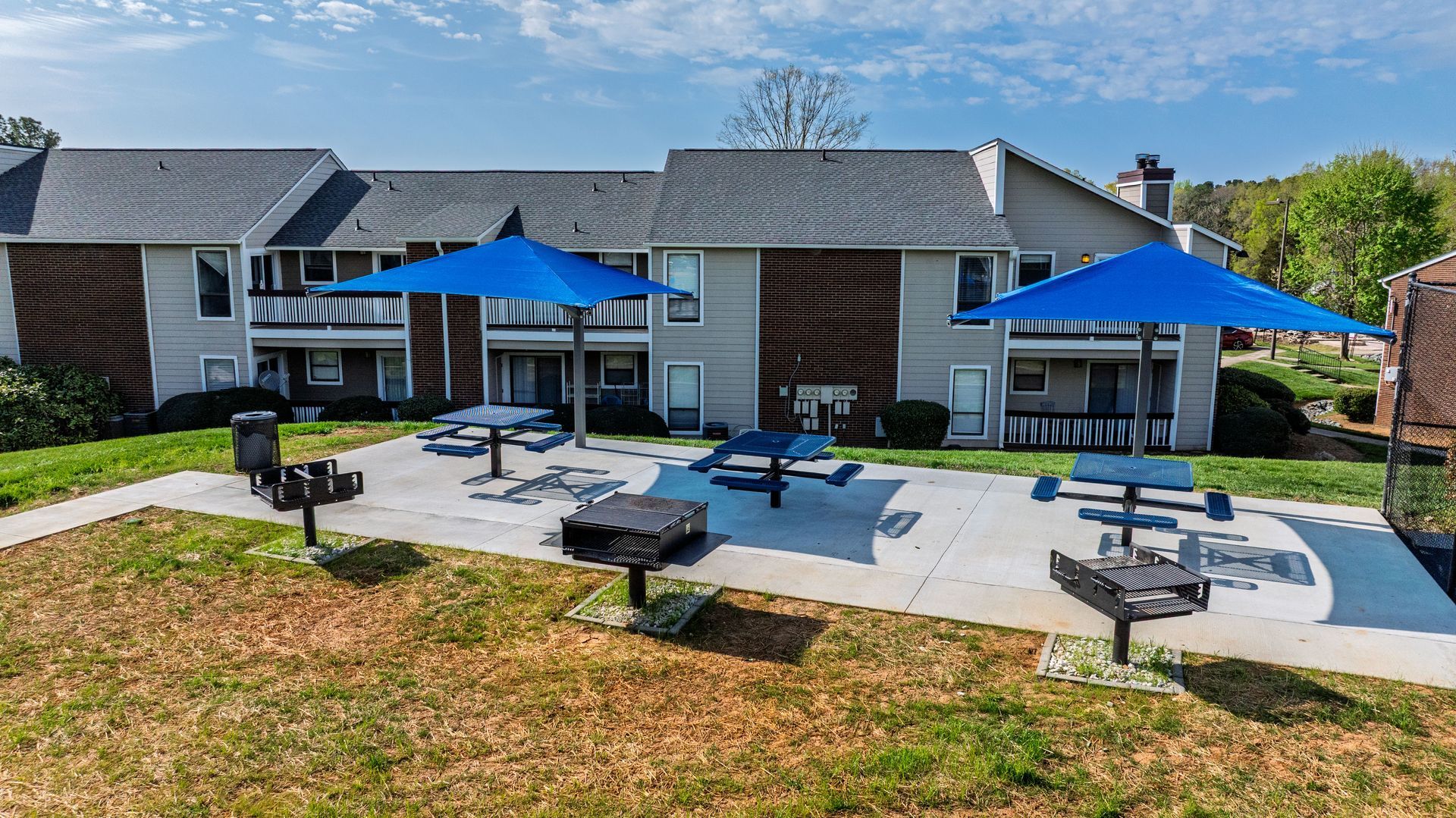 Apartment courtyard with blue umbrellas, tables, and outdoor seating on a sunny day