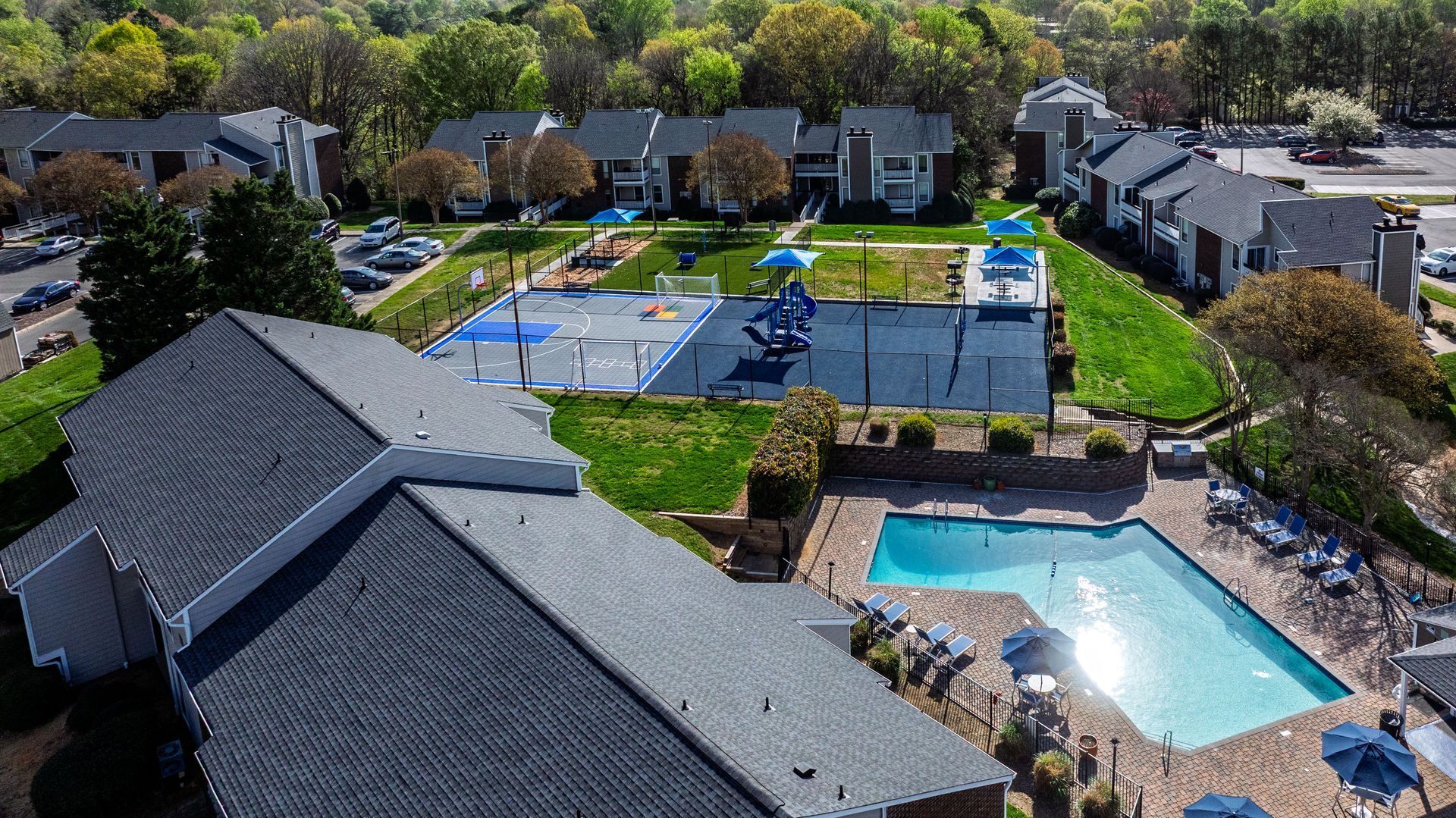 Aerial view of a suburban apartment complex with tennis courts and a swimming pool.