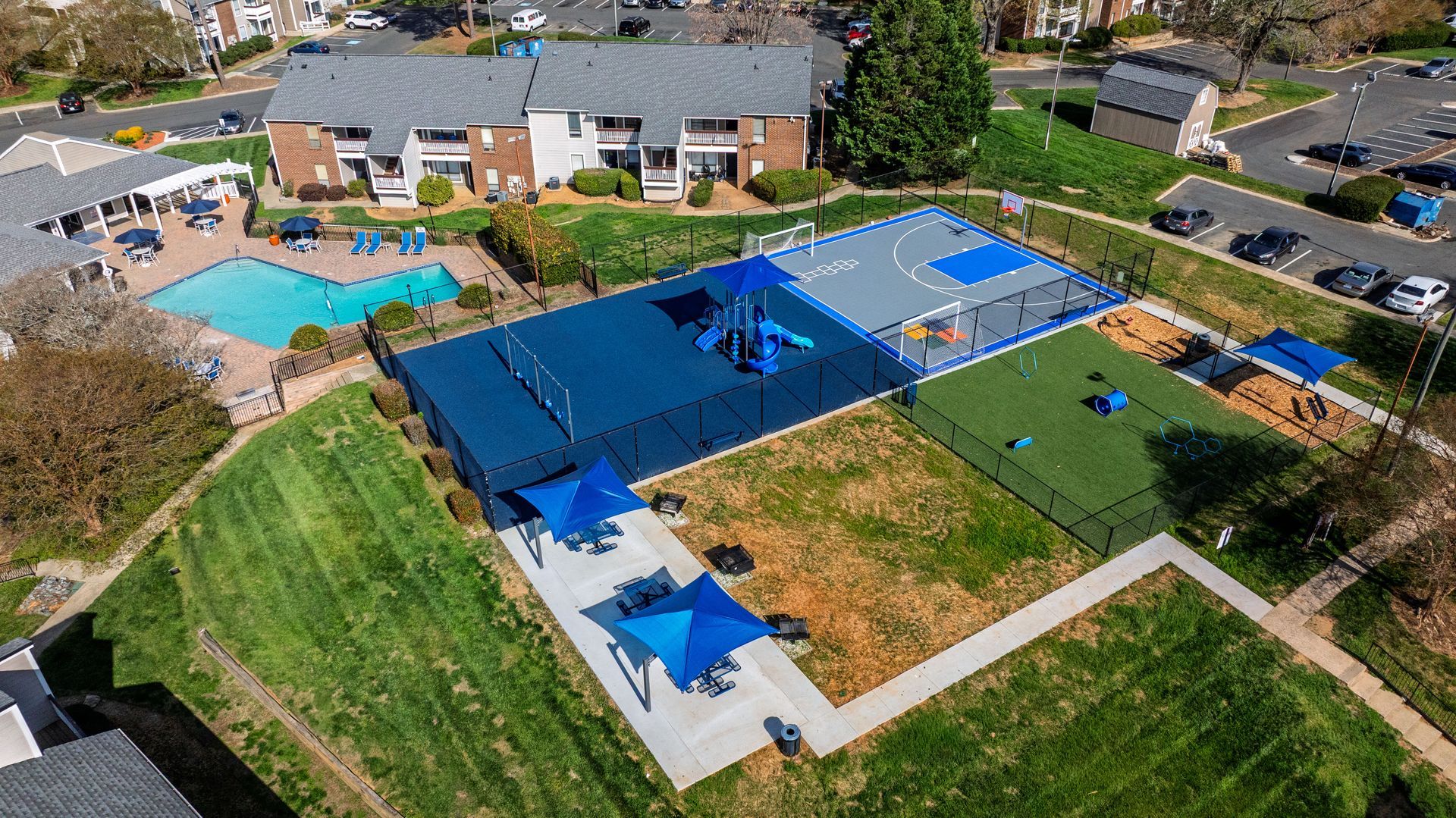 Aerial view of a school playground with blue shade sails, colorful play areas, and surrounding buildings