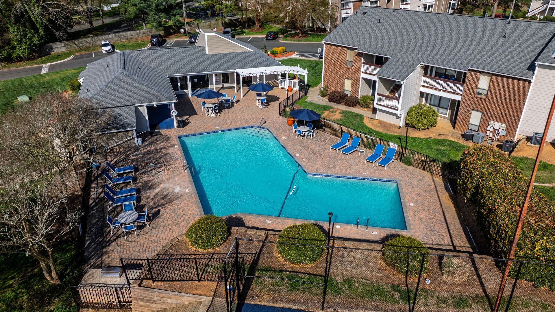 Outdoor swimming pool with blue lounge chairs beside brick apartment buildings and a covered seating area