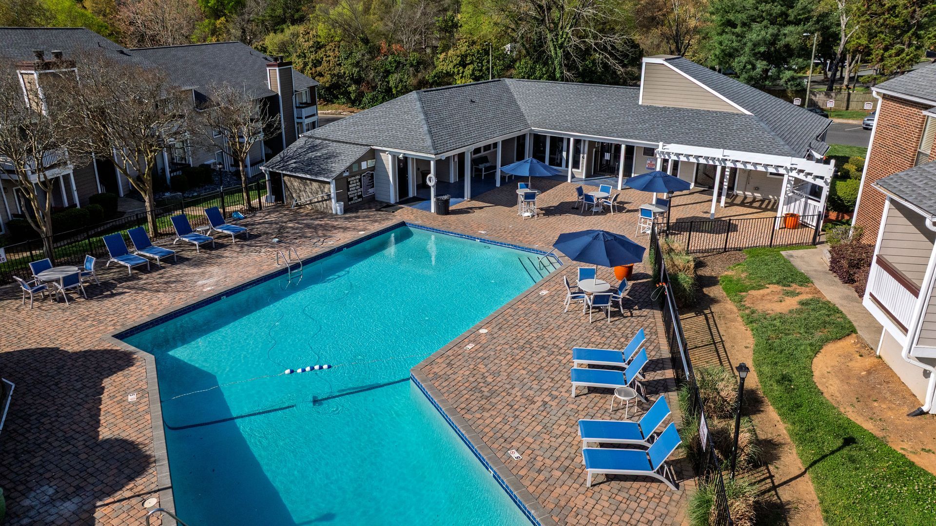 Outdoor pool with blue lounge chairs and umbrellas beside a clubhouse patio