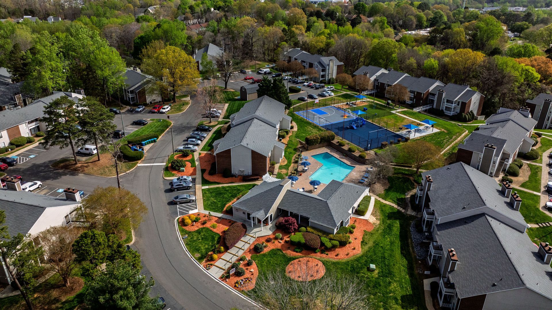 Aerial view of a suburban apartment complex with a central swimming pool, parking lots, and tree-lined roads
