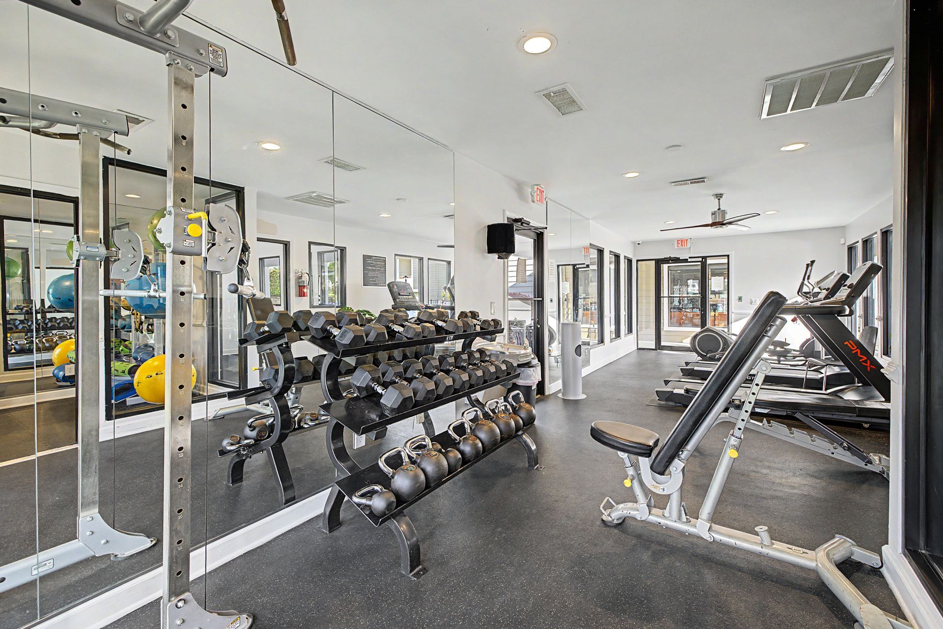 Bright gym interior with dumbbell racks, benches, mirrors, and exercise equipment