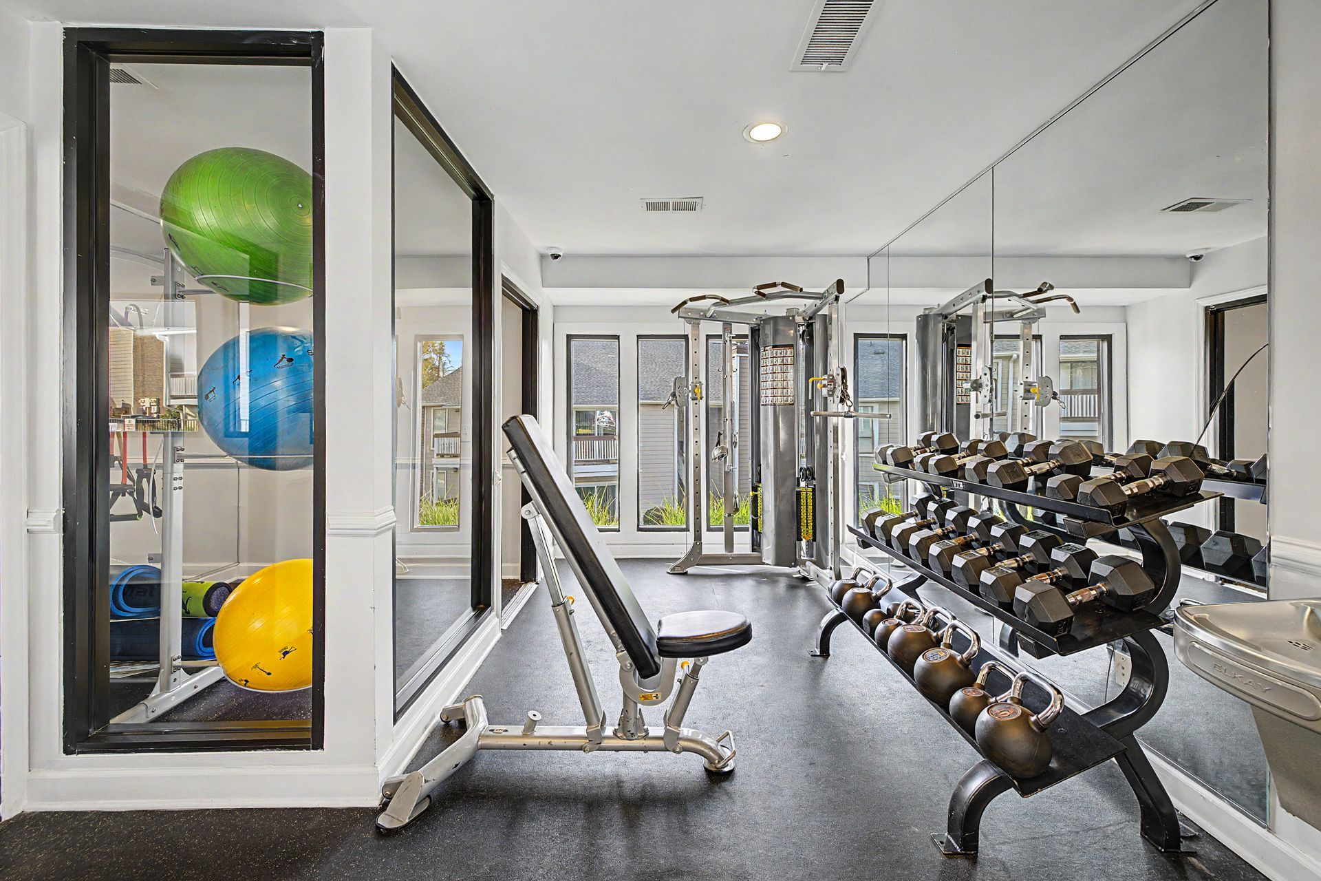 Modern gym with dumbbells, bench, mirrors, and colorful exercise balls in a storage rack